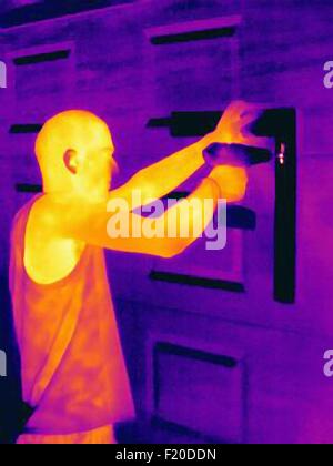 Thermal photograph of young man using a hand drill on cupboard Stock Photo