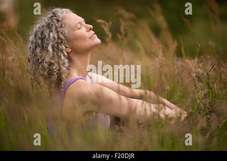Mature woman meditating in long grass Stock Photo