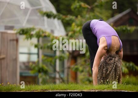Mature woman practicing yoga forward fold in eco lodge garden Stock Photo