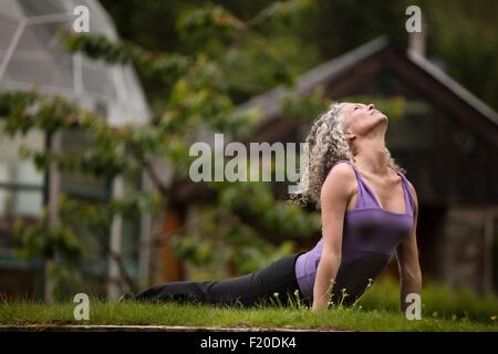 Mature woman practicing yoga upward dog in eco lodge garden Stock Photo