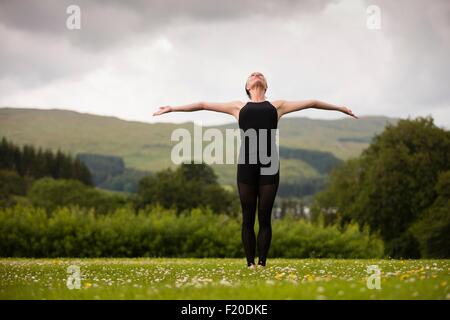 Mature woman practicing yoga position with arms open in field Stock Photo