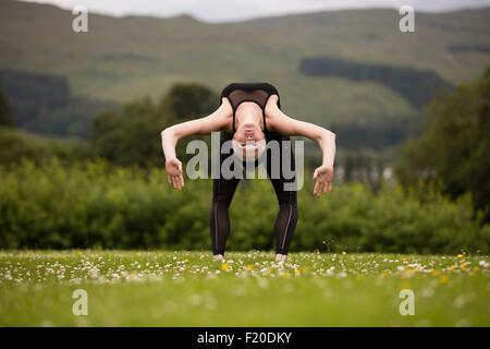 Mature woman practicing yoga bending backward in field Stock Photo