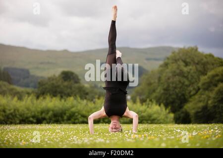 Mature woman practicing yoga standing on head with leg raised in field Stock Photo
