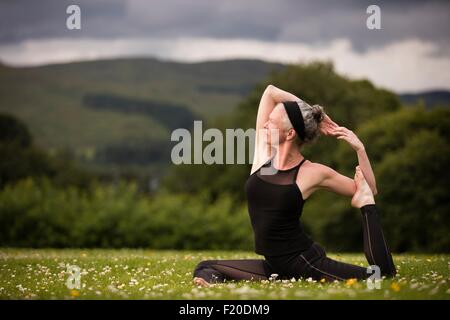 Mature woman doing splits practicing yoga in field Stock Photo