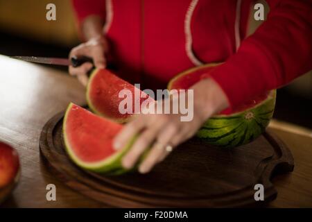 Cropped view of mature woman slicing watermelon in kitchen Stock Photo