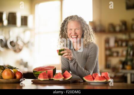 Portrait of mature woman eating watermelon in kitchen