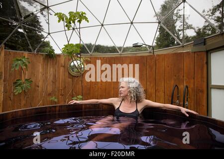 Mature woman relaxing in hot tub at eco retreat Stock Photo