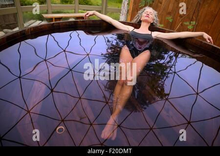 Mature woman lying back in hot tub at eco retreat Stock Photo