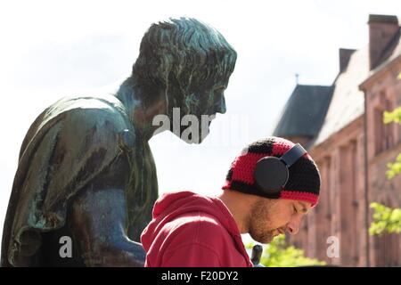 Head and shoulder portrait of mid adult man wearing headphones in front of sculpture, Freiburg, Baden, Germany Stock Photo