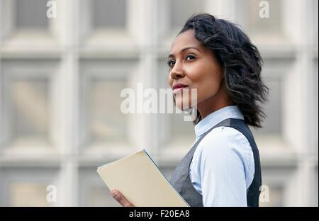 Portrait of young business woman holding paper work, looking away, side view Stock Photo