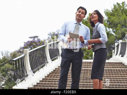 Business people standing in front of stairway holding digital tablet, looking up Stock Photo