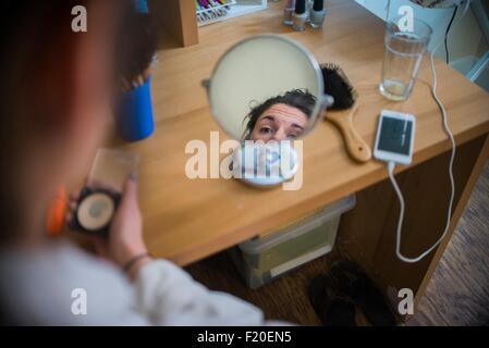 Young woman looking in mirror whist putting face make up on Stock Photo