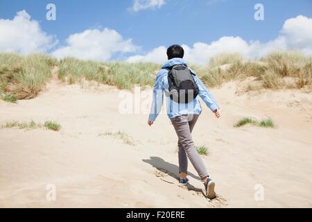 Rear view of mid adult female walker, walking up sand dune Stock Photo