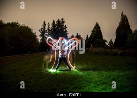 Young woman, standing in field at dusk, arms and legs outstretched in star shape, light trail tracing body shape Stock Photo