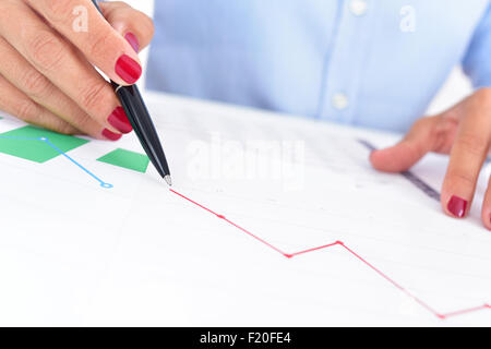 closeup of a businesswoman at her office desk full of graphs and charts, observes a chart with a downward trend Stock Photo