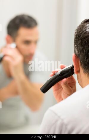 Mid adult man, looking in mirror, using electric shaver, rear view Stock Photo