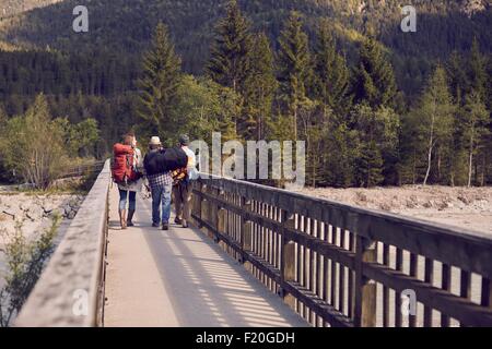 Rear view of three people walking to mountains wearing backpacks Stock Photo