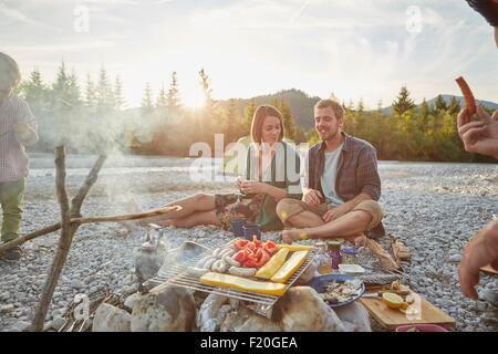 Family sitting around campfire cooking food on barbecue Stock Photo