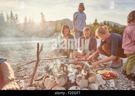 Family sitting around campfire preparing food Stock Photo