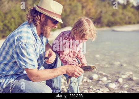 Mid adult man and boy next to river examining fish attached to fishing line Stock Photo
