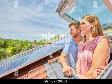 Young couple looking out of window of solar panelled roof Stock Photo