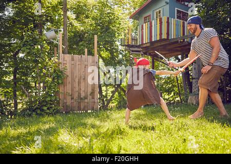 Father and son in garden, wearing costumes, playing with pretend swords Stock Photo