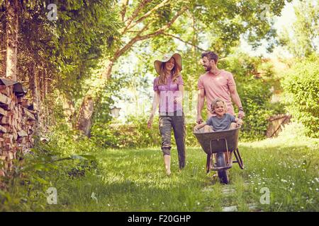 Young family outdoors, father pushing son in wheelbarrow Stock Photo