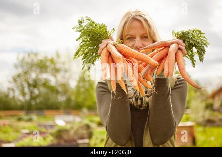 Portrait of mature woman, outdoors, holding two bunches of carrots Stock Photo