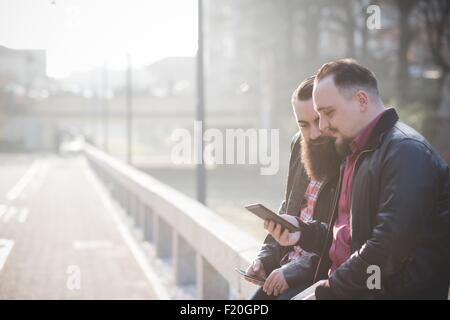 Gay couple using smartphone on pavement Stock Photo