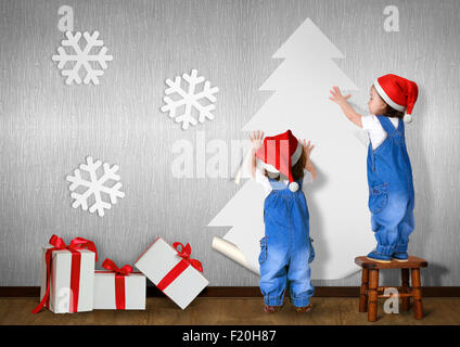 Little twins dressed Santa hat, glue Christmas tree on wall at home, xmas concept
