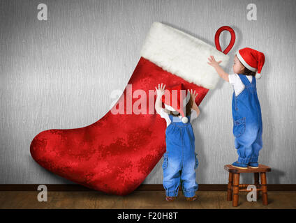 Little twins dressed Santa hat, hangs big Christmas stocking for gifts, xmas concept Stock Photo