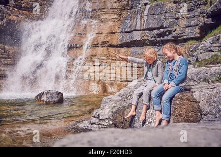 Brother and sister, sitting on rock, relaxing, beside waterfall Stock Photo