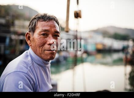 Portrait of senior man, side view, in front of boats on water, looking at camera Stock Photo
