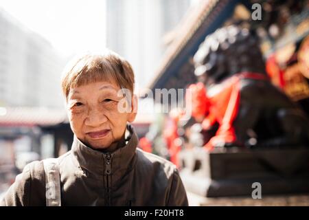 Portrait of senior woman wearing coat in front of lion statue, looking at camera Stock Photo