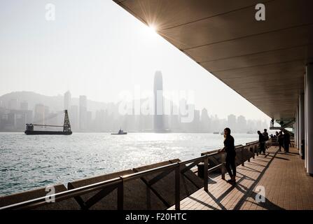 Silhouetted side view of young woman standing looking out over water at skyline, Hong Kong, China Stock Photo
