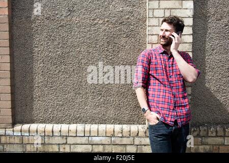 Young man leaning against wall chatting on smartphone Stock Photo