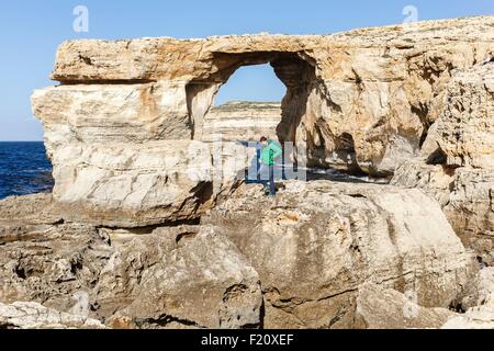 Malta, Gozo, Dwejra, Azure window, tourist on rocks in front of a natural arch in the cliff by the sea Stock Photo