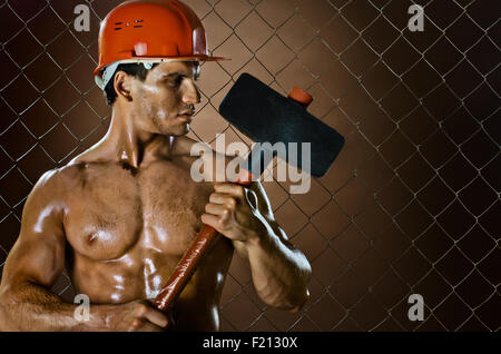 muscular worker , in  safety helmet  with big tup  in hands, on netting fence background Stock Photo