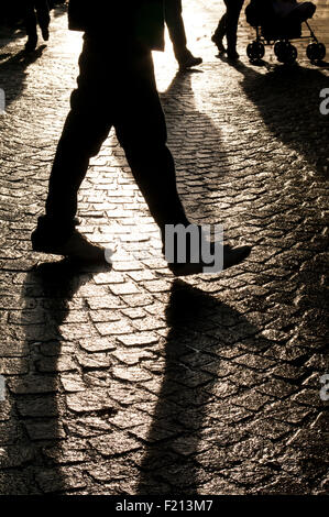 shadows and silhouettes of people walking on a backlit cobbled road in Bradford, Yorkshire Stock Photo