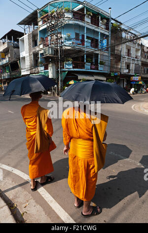 Laos, Vientiane, Two monks, shielded from sun by umbrellas, about to cross the street. Stock Photo