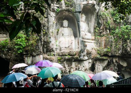 Tourists with umbrellas visiting Buddhas carved into rock face of Feilai Feng hill at Lingyin Temple Stock Photo