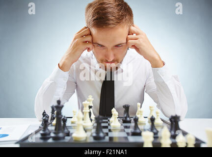 Pensive businessman in formalwear looking at chessboard while leaning over it Stock Photo