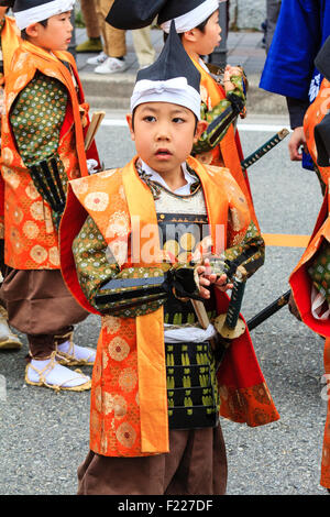 Genji Festival parade in Japan.Young child, boy, 8-10 year old, dressed as Shimobe soldier from the heian era. Standing, looking confused . Stock Photo