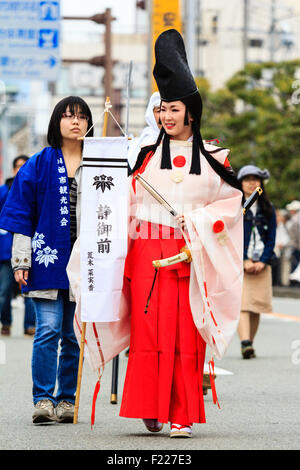 Genji festival parade in Tada, Japan. Young woman dressed as Heian shirabyoshi dancer, with long red skirt, white blouse, and tall black hat. Smiling. Stock Photo