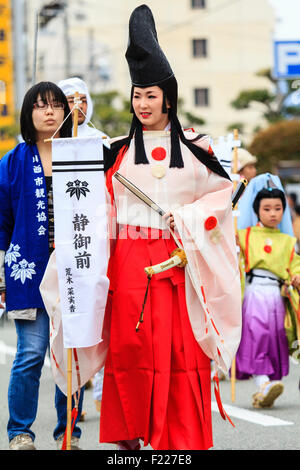 Genji festival parade in Tada, Japan. Young woman dressed as Heian shirabyoshi dancer, with long red skirt, white blouse, and tall black hat. Smiling. Stock Photo