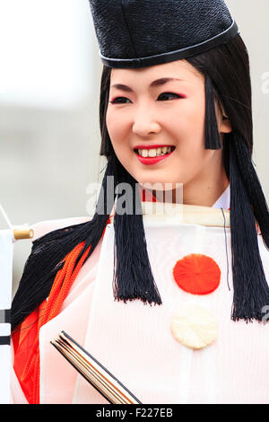 Genji festival parade in Tada, Japan. Young woman dressed as Heian shirabyoshi dancer, with long red skirt, white blouse, and tall black hat. Smiling. Stock Photo