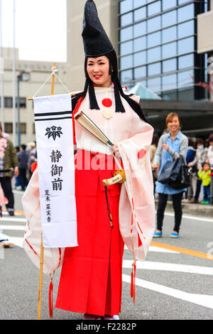 Genji festival parade in Tada, Japan. Young woman dressed as Heian shirabyoshi dancer, with long red skirt, white blouse, and tall black hat. Smiling. Stock Photo