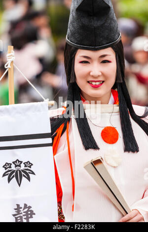 Genji festival parade in Tada, Japan. Young woman dressed as Heian shirabyoshi dancer, with long red skirt, white blouse, and tall black hat. Smiling. Stock Photo