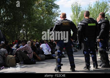 Hungarian policemen watch refugees, who shall be transported to a registration office by bus, at the refugee shelter Roeszke in Hungary, 9 September 2015. PHOTO: PETER ZSCHUNKE/dpa Stock Photo