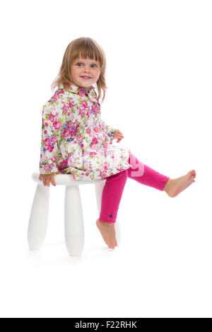 Little smiling girl sitting on a chair in the studio, isolate on white background. Stock Photo